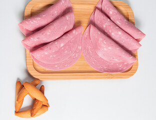 Slices of mortadella accompanied by slices of bread on a wooden board with a white background and a very bright base