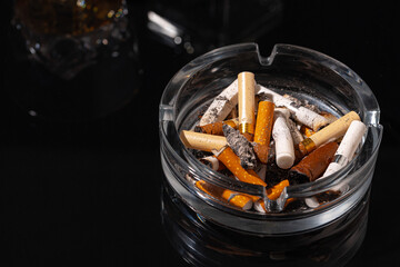 Ash tray full of cigarette butts on black background