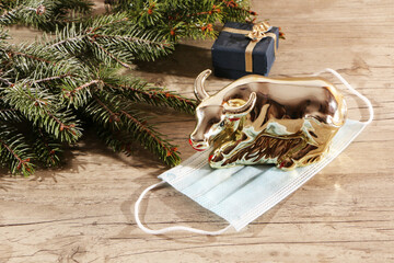  A metal bull stands on a medical mask as a symbol of the end of the pandemic in 2021, against the backdrop of a green Christmas tree.
