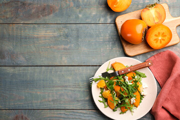 Delicious persimmon salad served on light blue wooden table, flat lay. Space for text