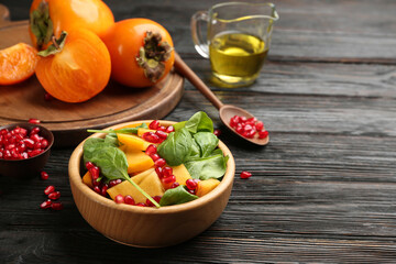Delicious persimmon salad with pomegranate and spinach on wooden table. Space for text
