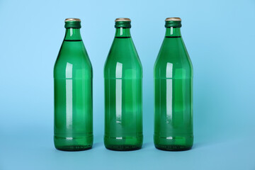 Glass bottles with water on light blue background