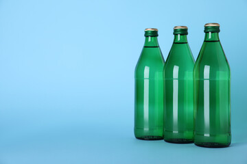 Glass bottles with water on light blue background, space for text