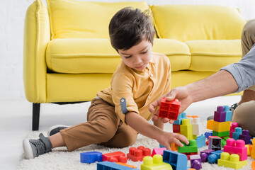 Boy sitting near father and colorful building blocks on blurred foreground at home, two generations of men