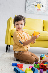 Fototapeta premium Boy holding building block and looking at camera near father, two generations of men