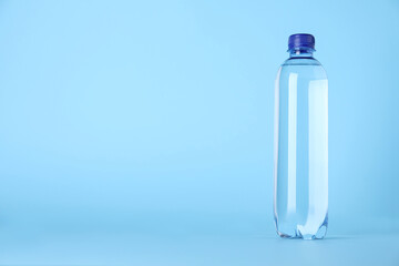 Plastic bottle with water on light blue background, space for text