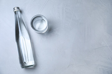 Glass and bottle with water on grey background, flat lay. Space for text