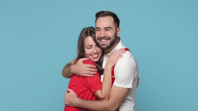 Smiling cheerful funny young couple friends bearded man woman 20s wearing white red clothes posing isolated on blue color wall background in studio. People sincere emotions lifestyle concept. Hugging
