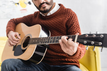 Cropped view of man performing acoustic guitar on couch on blurred background