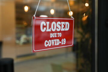 Red sign with words "Closed Due To Covid-19" hanging on glass door
