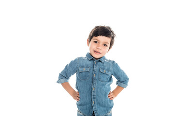 happy boy in denim shirt standing with hands on hips and looking at camera isolated on white