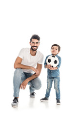 Obraz na płótnie Canvas happy boy holding soccer ball near cheerful hispanic father isolated on white, two generations of men