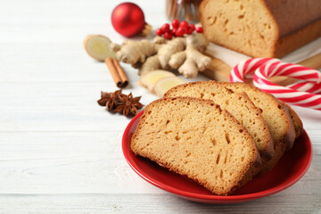 Slices of delicious gingerbread cake, ingredients and candy canes on white wooden table. Space for text