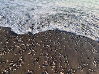 Sea water running on the sandy coastline with pebbles