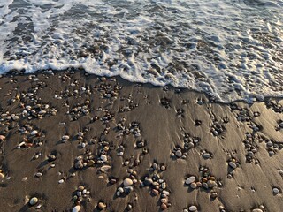 Sea water running on the sandy coastline with pebbles