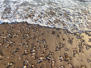 Sea water running on the sandy coastline with pebbles