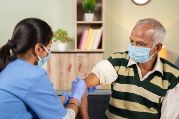 Doctor giving vaccination shot to elderly patient by syringe or injunction at home while both worj...
