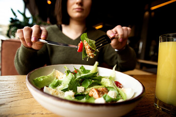 Caesar salad and glass of orange joice. Healthy food concept. Serious woman eating her meal. Restaurant or cafe on background. Diet concept. Young woman tired of eating just salads and vegetables.