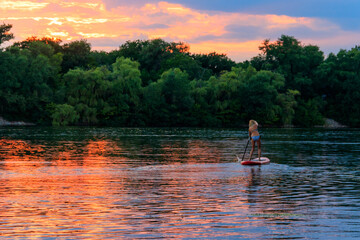 Fototapeta na wymiar Young woman on stand up paddle board (paddleboard, SUP) paddleboarding along the Dnieper river at sunset