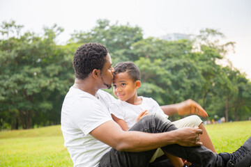 Happy African American father while hug and carry his son, Dad was kissing his son in the park, Joyful black family concept.