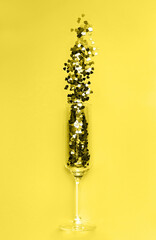 Trendy yellow heart-shaped confetti poured out of champagne glass. Flat lay. Love and celebration concept. Color 2021 concept.