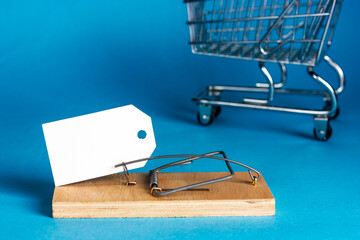 White paper plate in a wooden mousetrap on a blue background. Supermarket cart in the background....