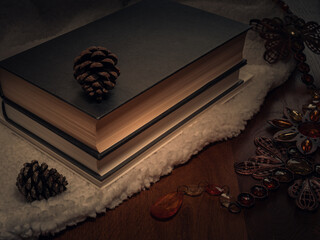 Hardback books on a white blanket with pine cones on a mahogany table