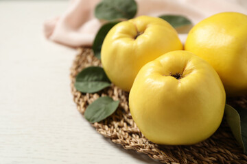 Fresh ripe organic quinces with leaves on white wooden table, closeup. Space for text