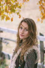 Outdoor portrait of woman standing near wooden fence in autumn mountain village forest