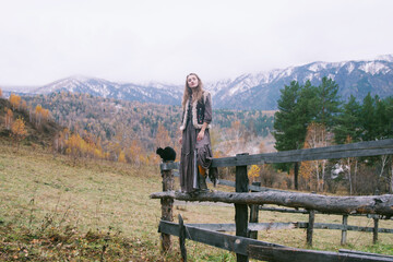 Fototapeta na wymiar Portrait of woman with black cat standing on wooden fence in autumn mountain village
