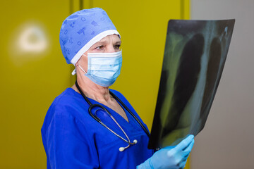 A surgeon in a surgical cap and a mask looking at an x-ray picture