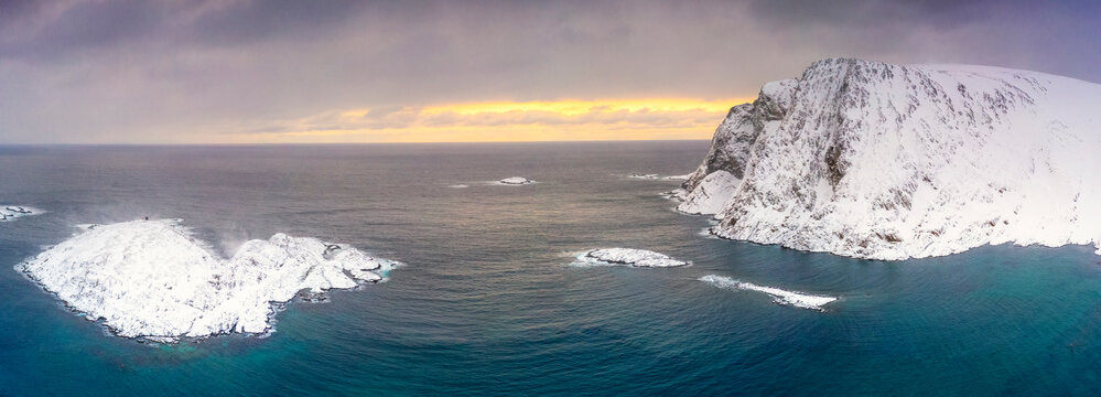 Waves of cold sea framed by snow capped mountains at dawn, aerial view, Sorvaer, Soroya Island, Hasvik, Troms og Finnmark, Arctic