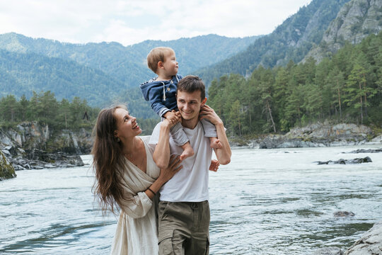 Young family father, mom and baby boy travel and walking  near mountain river, beautiful mountains landscape on background