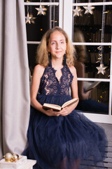A very beautiful teenage girl in a New Year's interior of an apartment or house near the window reads a book
