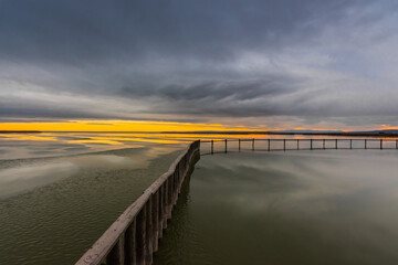 Fototapeta premium long wooden railing in a frozen lake with sun and rain clouds