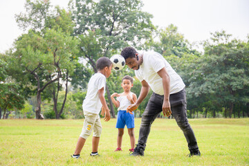 Fototapeta premium Cheerful african american father and two sons playing with football in park, Happiness family concepts