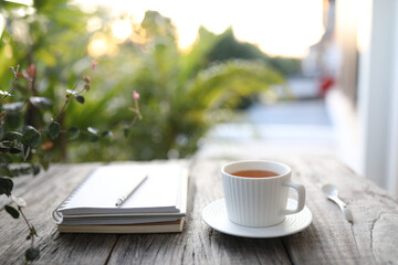 Tea in clay ceramic cup and notebooks and silver pen on wooden table 
