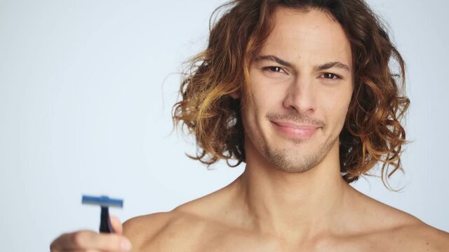 A confident man is throwing out a razor standing isolated over white wall in studio