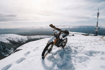 Enduro motocross Motorcycle on snow mountain top, off road, mountains peaks skyline on background
