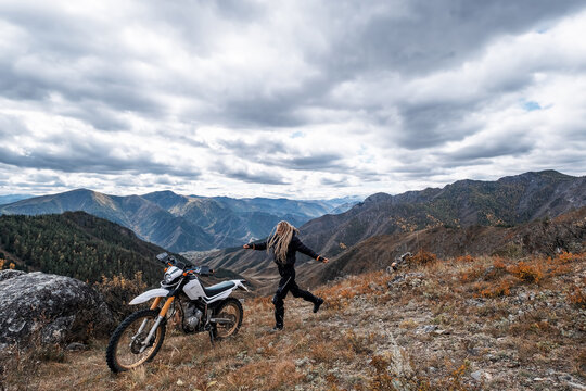 Young woman motorcyclist enjoying and rest on the mountain top with her enduro motorcycle. Off road motor traveling in wild mountains