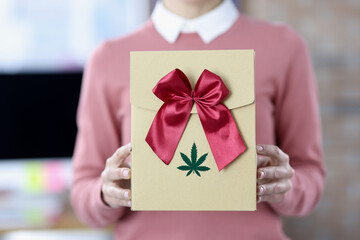Female hands hold box with bow and marijuana logo