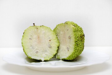 One ripe Maclura fruit cut in half with the appearance of seeds and milk juice (Latin Maclura), Mulberry family (Moraceae) on a white background