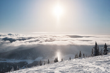 View from mountain top above clouds and sun in winter ski resort