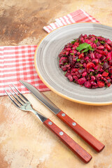 side close view of plate of a red salad with greens on it with checked napkin and the fork and knife at the side on a wooden backgorund
