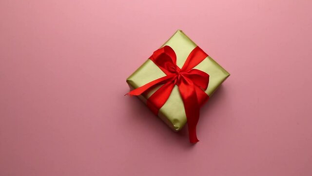 Festive gift in gold packaging and a red bow on a pink background. A pleasant gift and surprise for loved ones. High quality FullHD footage