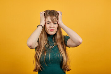 Headache grimacing pain holds the back of neck indicating location. Fatigue during workaholism labor. Young attractive woman, dressed green shirt blonde hair, yellow background