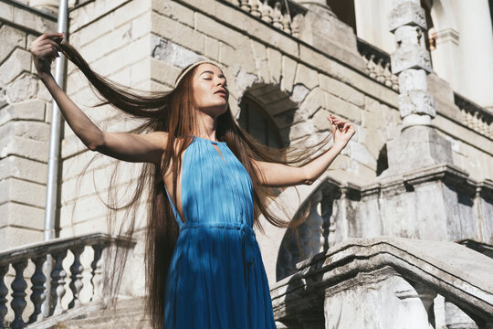 Beautiful woman with very long hair standing near antique building and dropping her hair with hands