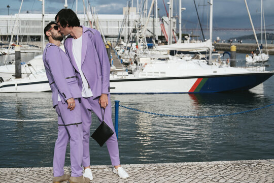 Romantic fashion homosexual male couple kissing on city beach, boats and yachts on background