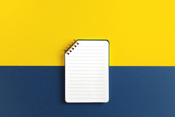 Blank ruled notepad on yellow and blue background. Top view, copy space.