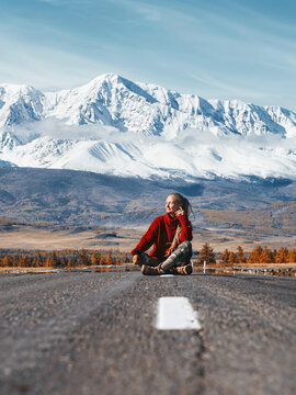 Traveling Woman seating on mountain road. Beautiful snowy peak on background. Travel concept